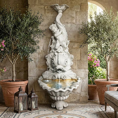 Decorative fountain with statues in a stone-walled room with plants and a sofa.