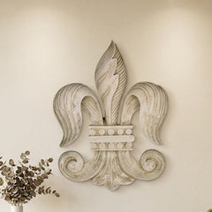 A large, ornate, textured light gray stone or concrete fleur-de-lis wall sculpture is mounted above a modern fireplace in a minimalist living room setting.