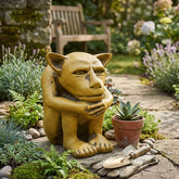 Garden gnome sitting on a stone path surrounded by plants and gardening tools.