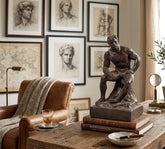 Statue on books on a wooden table with classical art and decor in the background
