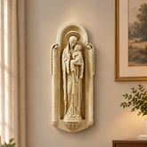 A beige stone-look religious wall sculpture of the Virgin Mary holding the infant Jesus, mounted on a warm beige wall in a styled living room with a sofa, sideboard, lamp, and framed artwork.