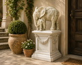Decorative stone elephant sculpture on a pedestal with potted plants in an outdoor setting.