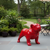 Red dog statue on a patio with garden and chairs in the background