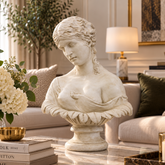An off-white classical-style bust sculpture of a woman with draped fabric, displayed on a marble coffee table in a beautifully decorated living room.