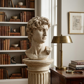 Bust on a pedestal in a room with books and a lamp