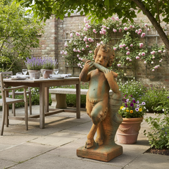Statue of a child playing a flute in a garden setting with a table and chairs.