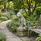 Garden scene with a stone cat statue and wooden bench surrounded by plants and flowers.