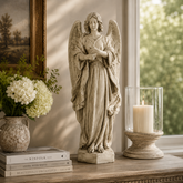 Statue of an angel on a table with books, flowers, and a candle