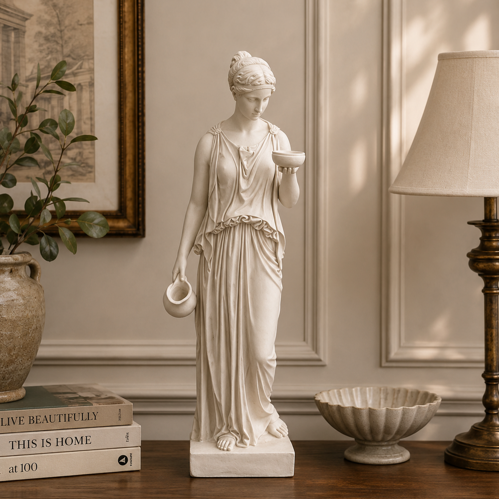 Statue of a classical woman holding a bowl on a wooden surface with books and decor items.