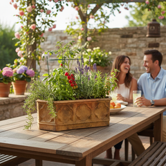 Couple sitting at an outdoor table with a large planter of herbs and flowers.