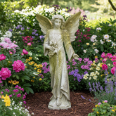 Statue of an angel holding flowers in a garden with colorful flowers