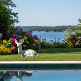Decorative deer figure on grass by a pool with flowers and trees in the background