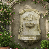 Decorative stone wall fountain with floral and greenery around