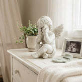 Nursery room with crib, statue, plant, and framed photo on a dresser.