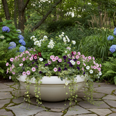 Floral arrangement in a white pot on a stone patio with greenery in the background