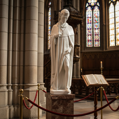 Sainted Peregrine Religious Sculpture Statue of a religious figure in a cathedral with stained glass windows and people in the background.