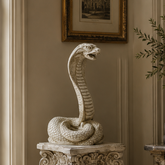 Decorative snake sculpture on a pedestal in an elegant room with a chair and table.