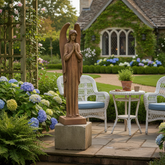 Wooden angel statue in a garden setting with chairs and flowers