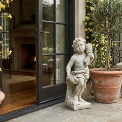 Statue of a cherub in a garden setting with potted plants and a door in the background Summer Season Cherub 24" H Statue