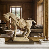 Decorative horse sculpture on a marble fireplace mantel with books and a vase.
