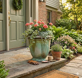 Decorative potted plants on a stone porch with a green door and garden in the background.