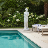 Statue by a pool with lounge chairs and a garden in the background