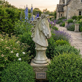 Stone horse head sculpture in a garden with a house in the background