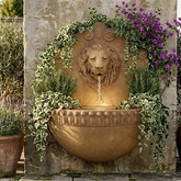 Decorative stone lion-head fountain with plants in a garden setting
