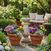 Garden scene with terracotta pots filled with colorful flowers, a stone sundial, and outdoor seating.