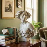 Bust on a wooden desk with books and decorative items against a green wall.