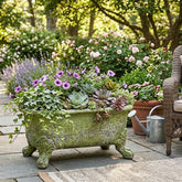 Decorative garden with potted plants, including a moss-covered bathtub planter, on a stone patio.