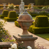 Decorative garden with potted plants and a stone urn in a formal garden setting.