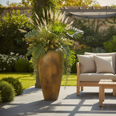 Outdoor patio setting with a sofa, coffee table, and large planter in a garden.