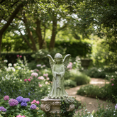 Statue of an angel in a garden with flowers and trees