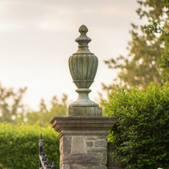 Decorative garden gate with stone pillars and white flowers on a sunny day.
