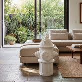 Living room with a white fire hydrant sculpture, beige sofa, and large glass door leading to a garden.