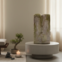A serene interior setting with a stone sculpture, small tree, and candles on a rug.