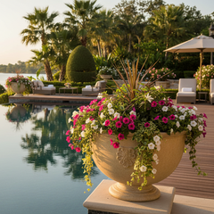 Decorative urn with flowers by a poolside with palm trees and lounge chairs.