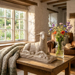 Decorative sheep sculpture on a wooden table with a vase of flowers in a rustic room.