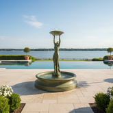 Fountain with a statue of a woman holding a lantern in front of a pool and lake.