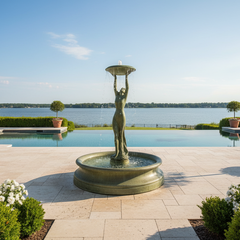 Fountain with a statue of a woman holding a lantern in front of a pool and lake.