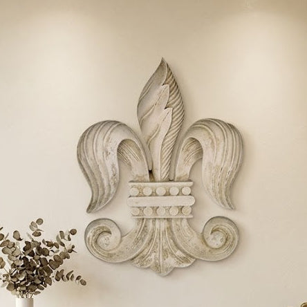 A large, ornate, textured light gray stone or concrete fleur-de-lis wall sculpture is mounted above a modern fireplace in a minimalist living room setting.