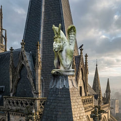 Gothic cathedral with detailed architecture and a statue on top against a cloudy sky.