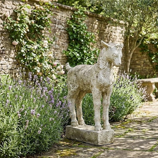 Stone goat sculpture in a garden setting with lavender and a stone wall.