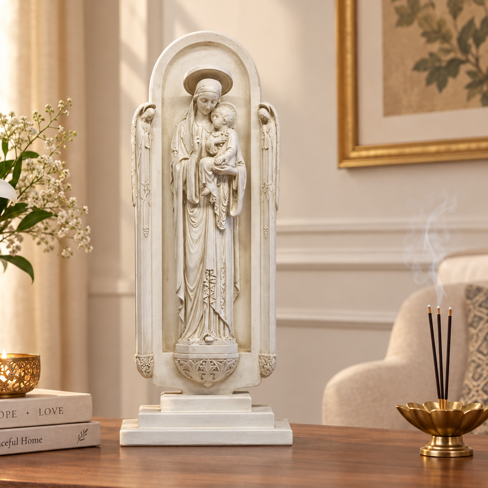An off-white stone-look religious statue of the Virgin Mary holding baby Jesus, displayed on a wooden table in a beautifully decorated room with a vase of lilies, books, and an incense burner.