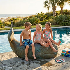 Children sitting on a stone sculpture by a pool with palm trees in the background