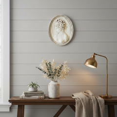 Decorative wall piece above a wooden table with a lamp and plants against a gray paneled wall.