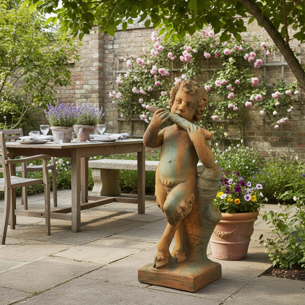 Statue of a child playing a flute in a garden setting with a table and chairs.
