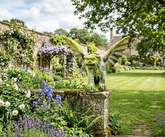 Gargoyles on stone pillars in a lush garden with flowers and trees