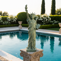 Statue of Liberty replica on a pedestal by a pool with garden in the background